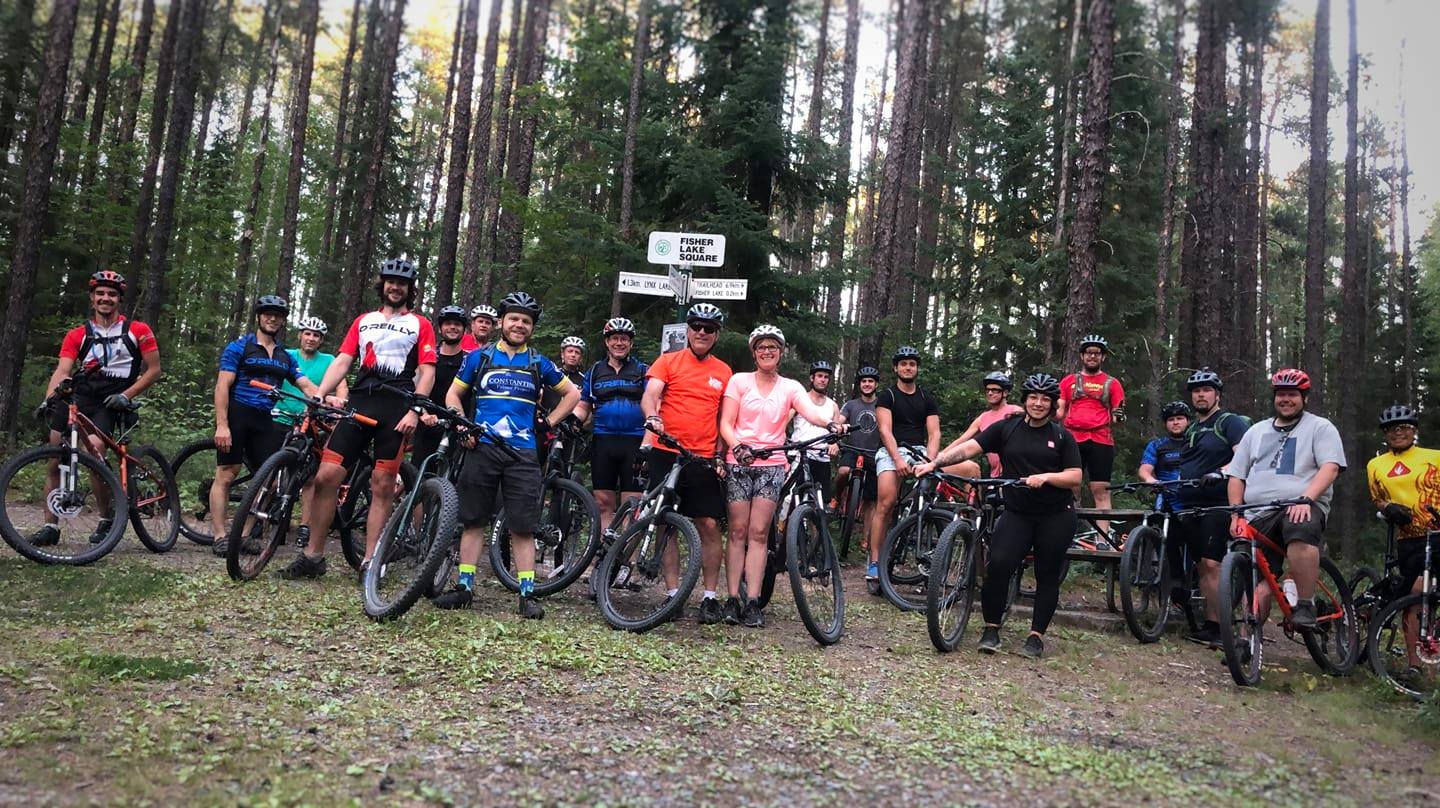 Group photo of mountain bikers by a trail sign.